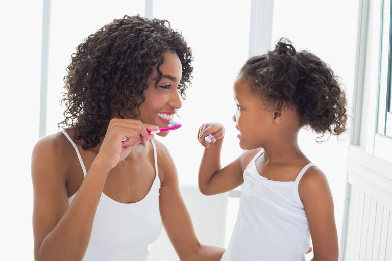 Mother and daughter brushing their teeth together with fluoride toothpaste at home